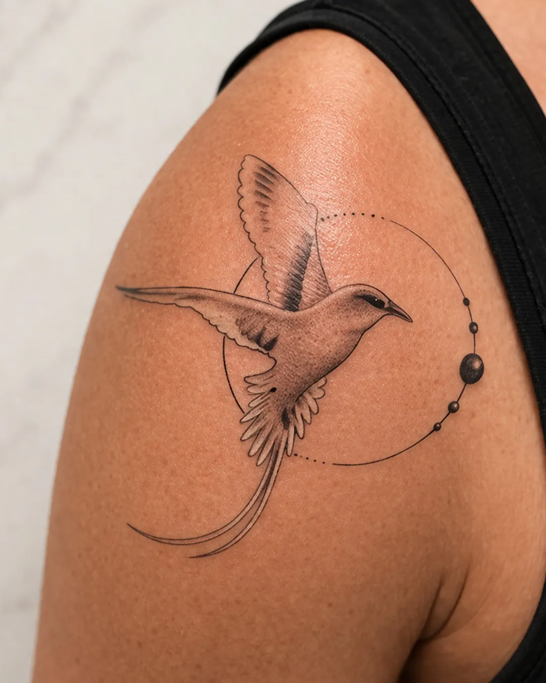 Oiseau en vol traversant un cercle ponctué de perles, trait fin, sur l’épaule
